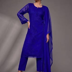 Puede incluir: Un vibrante conjunto de tres piezas en azul real que consta de una t&uacute;nica de manga larga con intrincados bordados tonales, un pantal&oacute;n de corte recto a juego y una dupatta ligera y transparente con un delicado borde de encaje festoneado.