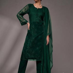 Puede incluir: Una t&uacute;nica de manga larga en color verde esmeralda oscuro con intrincados bordados tonales en el corpi&ntilde;o y las mangas, combinada con pantalones rectos a juego y un dupatta ligero y transparente con un borde de encaje festoneado.