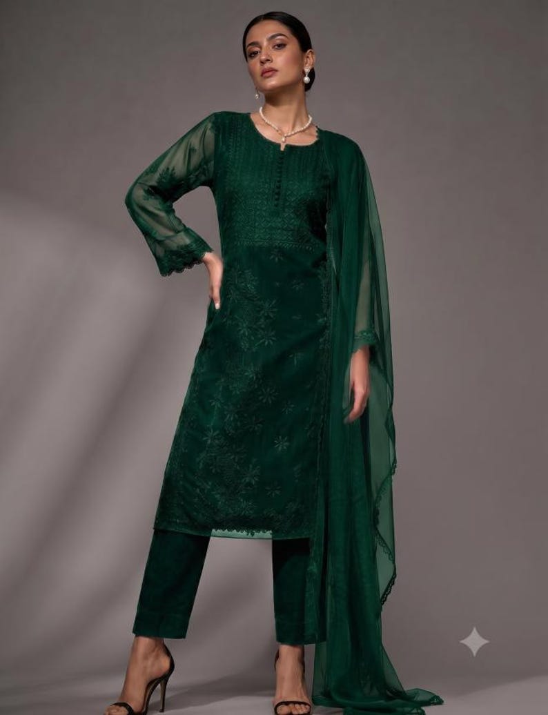 Puede incluir: Una t&uacute;nica de manga larga en color verde esmeralda oscuro con intrincados bordados tonales en el corpi&ntilde;o y las mangas, combinada con pantalones rectos a juego y un dupatta ligero y transparente con un borde de encaje festoneado.