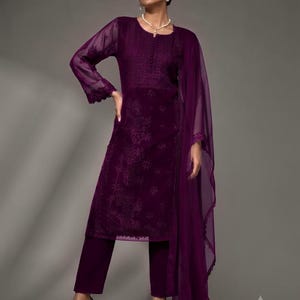 Puede incluir: Una t&uacute;nica de manga larga en color morado intenso con intrincados bordados tonales en el corpi&ntilde;o y las mangas, combinada con pantalones rectos a juego y un dupatta ligero y transparente con un borde de encaje festoneado sobre el hombro.