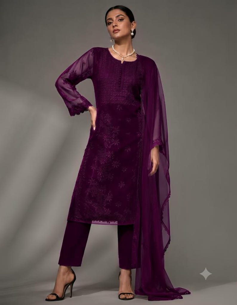 Puede incluir: Una t&uacute;nica de manga larga en color morado intenso con intrincados bordados tonales en el corpi&ntilde;o y las mangas, combinada con pantalones rectos a juego y un dupatta ligero y transparente con un borde de encaje festoneado sobre el hombro.