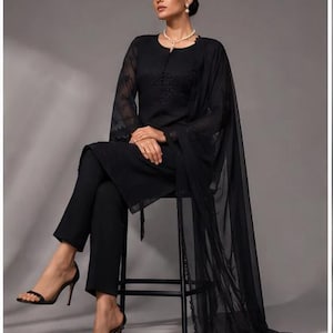 Puede incluir: Un conjunto negro de tres piezas que consta de una t&uacute;nica de manga larga con intrincados bordados tonales en el corpi&ntilde;o y mangas transparentes, pantalones ajustados a juego y un dupatta negro largo, ligero y semitransparente.
