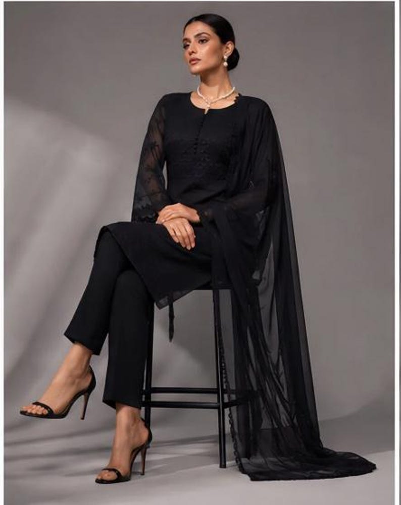 Puede incluir: Un conjunto negro de tres piezas que consta de una t&uacute;nica de manga larga con intrincados bordados tonales en el corpi&ntilde;o y mangas transparentes, pantalones ajustados a juego y un dupatta negro largo, ligero y semitransparente.