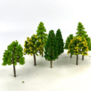 May include: A collection of miniature model trees in varying shades of green and yellow. The trees have brown trunks and are arranged against a white background. The foliage is detailed, suggesting a variety of tree types, perfect for model landscapes.