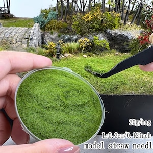 May include: A clear circular container filled with vibrant green static grass for model dioramas. The text on the image indicates 20g/bag and a length of 0.3 cm or 0.12 inches for the model straw needle grass fibers used in landscaping.