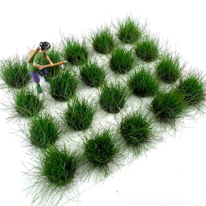 May include: A collection of miniature green grass tufts, ideal for model scenery. The grass is a vibrant green color, and the tufts are arranged in a grid pattern. A miniature figure is working with a tool in the grass.