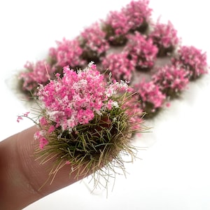 May include: Close-up of miniature pink and white flowering bushes with green grass-like bases. Several similar bushes are in the background. These small, detailed plants are likely for model scenery or crafts.