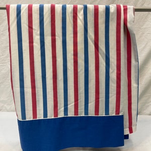 May include: A white fabric with red and blue stripes. The fabric has a blue trim at the bottom.