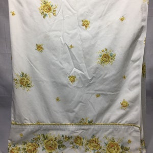 Puede incluir: Sábana bajera blanca con un estampado floral de rosas amarillas. La sábana tiene un borde decorativo con un estampado floral de rosas amarillas.