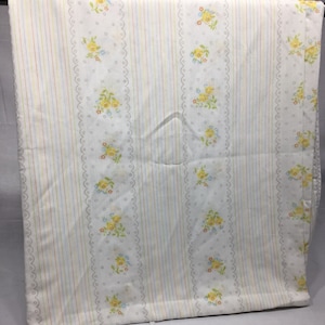 May include: White fabric with a striped pattern and a floral design. The stripes are in shades of yellow, orange, and blue. The floral design features small yellow flowers with blue and orange accents.