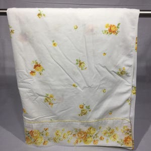 Op de afbeelding: Wit hoeslaken met een geel en oranje bloemenpatroon. Het laken heeft een rand van kleinere bloemen.