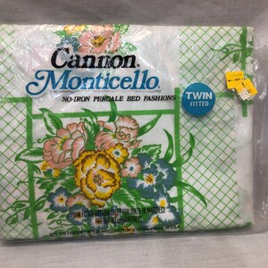 Puede incluir: Una sábana bajera blanca de tamaño twin con un patrón de cuadros verdes y blancos y un diseño floral. La sábana está hecha de 50% poliéster y 50% algodón peinado. El embalaje dice "Cannon Monticello No-Iron Percale Bed Fashions".