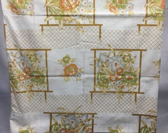 Pode incluir: Tecido branco com um padrão floral. As flores são laranja, verde e azul. O tecido tem um padrão de grade em dourado.