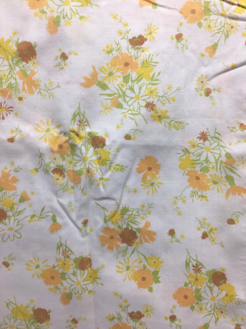 Pu&ograve; includere: Tessuto bianco con un motivo floreale con fiori gialli, arancioni e marroni. I fiori sono disposti a grappoli e sono sparsi sul tessuto.