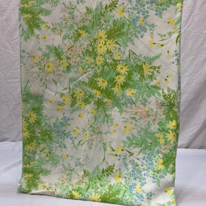 May include: A white fabric with a floral pattern featuring yellow, green, and blue flowers. The fabric has a vintage feel and would be perfect for a tablecloth or curtains.