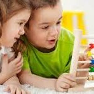 May include: Two children, a boy and a girl, are looking at a wooden abacus with colorful beads. The abacus has a series of horizontal rods with beads in various colors, including red, blue, yellow, and white. The children are wearing green shirts.