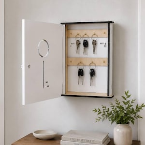 Könnte beinhalten: Ein weißer Schlüsselhalter mit einem schlüsselförmigen Ausschnitt an der Tür, an der Wand befestigt. Im Inneren befinden sich Holzleisten mit Schlüsseln. Der Schlüsselhalter ist geöffnet und zeigt die Schlüssel. Ein Holztisch darunter enthält Bücher und eine Vase.
