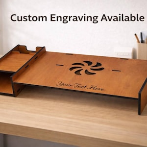 以下が含まれることがあります： 明るい茶色の木製デスクオーガナイザー。左側にコンパートメントがあり、装飾的な切り抜きのあるメインの表面があります。「Custom Engraving Available」と「Your Text Here」の文字が見えます。
