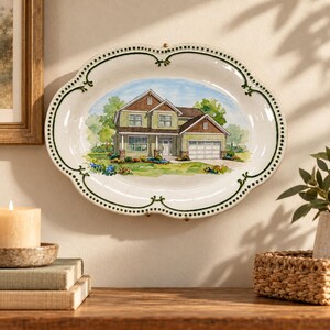 Pode incluir: Uma travessa oval de cerâmica com uma ilustração em aguarela pintada à mão de uma casa de dois andares com revestimento verde, telhado castanho e garagem. A travessa tem uma borda recortada com uma moldura verde-escura e pontos.
