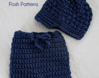 Könnte beinhalten: Ein gehäkeltes Baby-Outfit in Marineblau, bestehend aus Mütze und Hose. Die Mütze hat ein strukturiertes Stichmuster, während die Hose ein einfaches Stichmuster hat. Das Outfit ist aus weichem Garn gefertigt und perfekt für ein Neugeborenes.