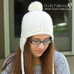 Puede incluir: Gorro de punto blanco con un pompón en la parte superior y orejeras largas. El gorro lo lleva una persona con el pelo largo y castaño y gafas.