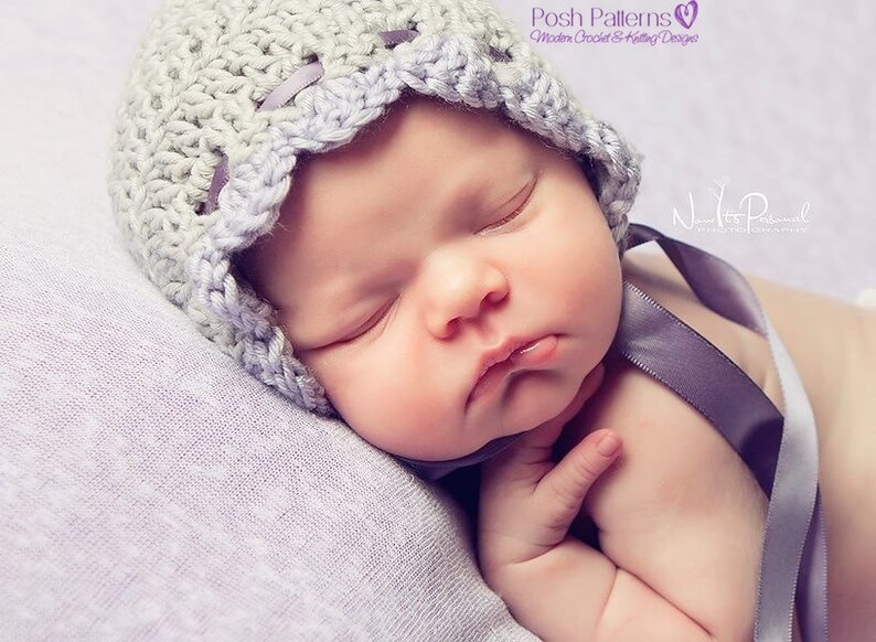 May include: A baby wearing a crocheted bonnet with a scalloped edge in a light gray color. The baby is sleeping on a soft, purple blanket. The bonnet has a satin ribbon tied around the back.
