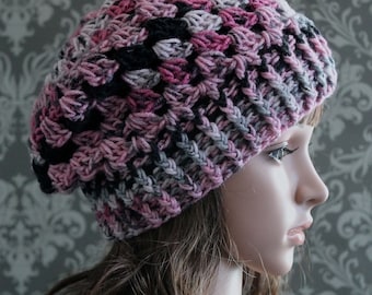 Könnte beinhalten: Eine gestrickte Mütze in Rosa, Grau und Schwarz. Die Mütze hat eine lockere Passform und ist mit einem strukturierten Stich gearbeitet.