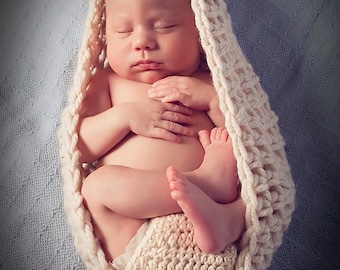 Könnte beinhalten: Ein neugeborenes Baby, das in eine weiße Häkeldecke gewickelt ist. Das Baby schläft friedlich mit gekreuzten Armen und eingezogenen Beinen. Die Decke ist mit einem einfachen Stichmuster gearbeitet und hat ein weiches, gemütliches Aussehen.