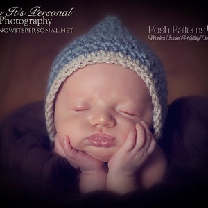 Może przedstawiać: Śpiące dziecko w niebiesko-białym kapeluszu na szydełku. Kapelusz ma spiczasty wierzchołek i biały brzeg. Dziecko ma na sobie brązowy kocyk.