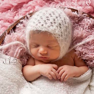 May include: A newborn baby wearing a white crocheted bonnet, sleeping peacefully in a pink fluffy basket.
