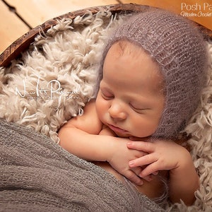 Puede incluir: Un bebé durmiendo con un gorro de crochet morado claro, acostado sobre una superficie blanca y esponjosa dentro de un cuenco de madera.
