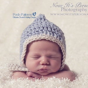 May include: A baby wearing a light blue and white crocheted hat with a pointed top. The baby is sleeping with its arms crossed in front of its face. The baby is lying on a white fluffy surface.