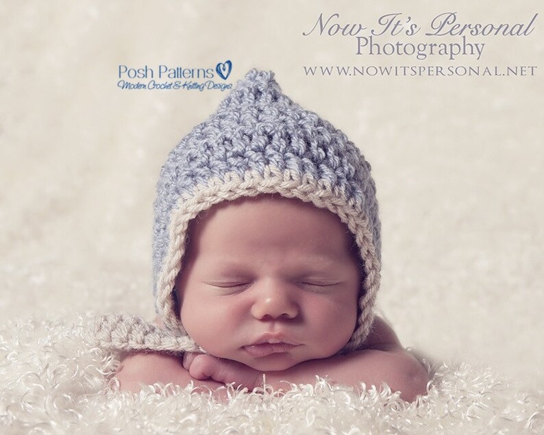 May include: A baby wearing a light blue and white crocheted hat with a pointed top. The baby is sleeping with its arms crossed in front of its face. The baby is lying on a white fluffy surface.