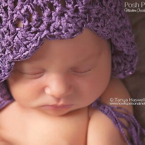 May include: A close-up of a sleeping baby wearing a purple crocheted bonnet. The baby's eyes are closed and their mouth is slightly open. The bonnet has a scalloped edge and is tied with a long purple ribbon.