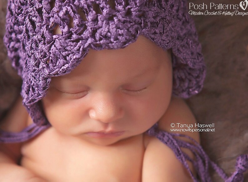 May include: A close-up of a sleeping baby wearing a purple crocheted bonnet. The baby's eyes are closed and their mouth is slightly open. The bonnet has a scalloped edge and is tied with a long purple ribbon.