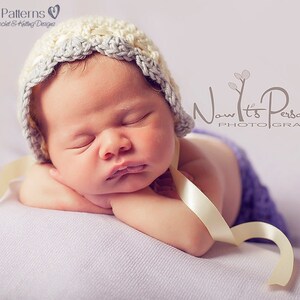 May include: A sleeping baby wearing a white and gray crocheted hat with a cream satin ribbon tied around the hat. The baby is lying on a purple blanket.