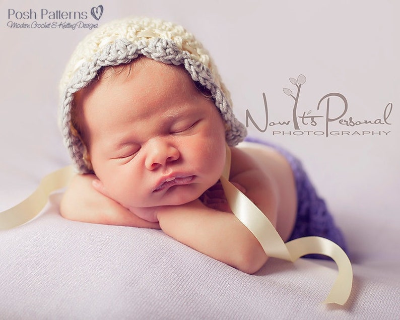 May include: A sleeping baby wearing a white and gray crocheted hat with a cream satin ribbon tied around the hat. The baby is lying on a purple blanket.