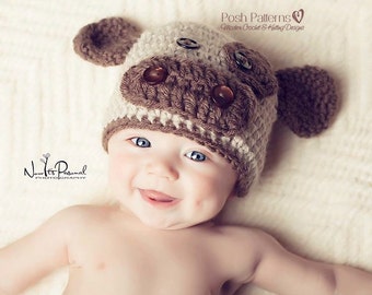 Puede incluir: Un bebé con un gorro de punto marrón y blanco en forma de cachorro con ojos de botón marrones. El gorro tiene orejas caídas y una nariz marrón.