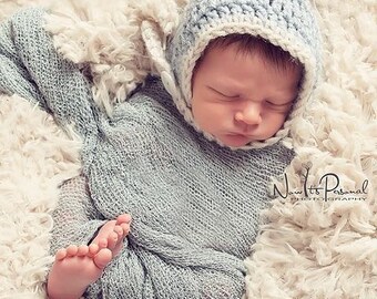 Puede incluir: Un bebé recién nacido con un gorro de ganchillo azul claro con ribete blanco. El gorro tiene una punta puntiaguda y un botón en el lateral. El bebé está durmiendo en una manta blanca y esponjosa.