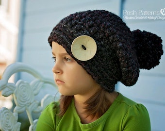 May include: A young person wearing a black and grey crocheted beanie with a large wooden button. The beanie has a pom-pom on top. The person is wearing a green shirt.