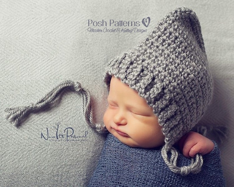 May include: A gray crocheted baby hat with a long, tied tassel. The hat has a pointed top and covers the ears. The hat is worn by a sleeping baby.