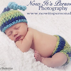Puede incluir: Un bebé durmiendo con un gorro y un pañal de crochet azul, verde y amarillo. El bebé está acostado sobre una manta blanca y esponjosa. El texto "Now It's Personal Photography" y "www.nowitspersonal.net" es visible sobre el bebé.