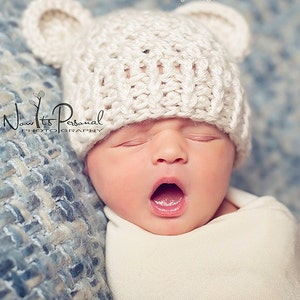 May include: A newborn baby wearing a cream-colored crocheted bear hat with ears, wrapped in a white blanket. The baby is yawning with its mouth open. The background is a blue and gray textured blanket. The image has the text "Posh Patterns" and "Modern Crochet & Knitting Designs".