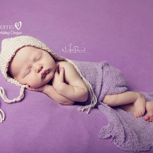 Peut inclure: Un bébé endormi portant un bonnet en crochet blanc avec un long pompon, enveloppé dans une couverture en tricot lavande sur un fond violet.
