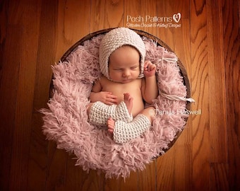 Puede incluir: Un bebé recién nacido con un gorro blanco de ganchillo y polainas a juego, durmiendo en una cesta rosa peluda. El bebé lleva un gorro blanco de ganchillo y polainas a juego. El bebé está durmiendo en una cesta rosa peluda. La cesta está sentada en un suelo de madera.