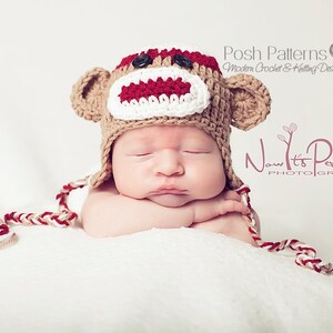 May include: A newborn baby wearing a crocheted monkey hat with red, white, and brown yarn. The hat has a button nose and a red mouth.