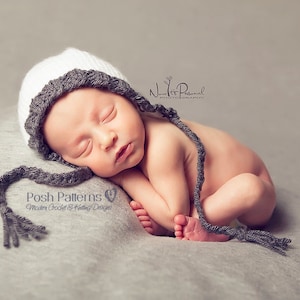 May include: A newborn baby wearing a white and grey knitted hat with a long grey tassel. The baby is sleeping on a grey blanket.
