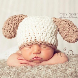 May include: A newborn baby wearing a white and brown crocheted hat with floppy ears. The hat has the text "Posh Patterns Modern Crochet & Knitting Designs" on the side.
