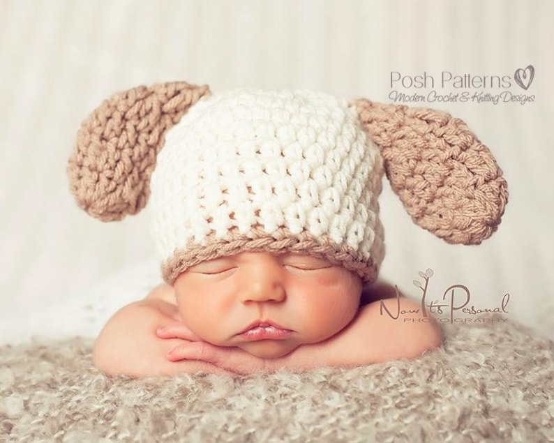 May include: A newborn baby wearing a white and brown crocheted hat with floppy ears. The hat has the text "Posh Patterns Modern Crochet & Knitting Designs" on the side.