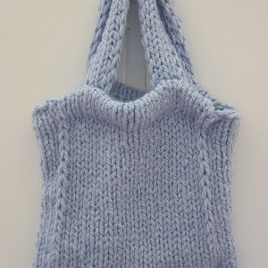 K&ouml;nnte beinhalten: Eine hellblaue gestrickte Einkaufstasche mit einem breiten, flachen Boden und zwei dicken Henkeln. Die Tasche ist mit einem einfachen Stichmuster gearbeitet und hat eine leicht strukturierte Oberfl&auml;che.